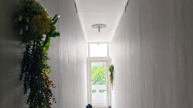 A hallway with white walls, a tiled floor, and hanging plants on either side. - Ez Door (Yogyakarta)