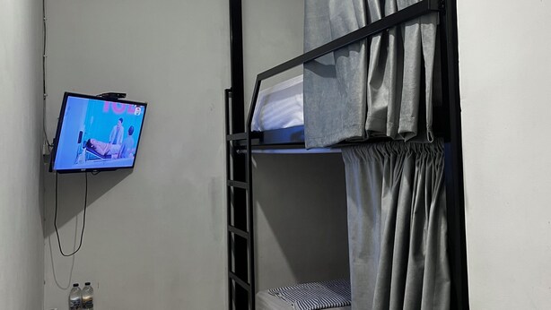 A bunk room with a television mounted on the wall, a small table with bottled water, and a ladder. - Ez Door (Yogyakarta)