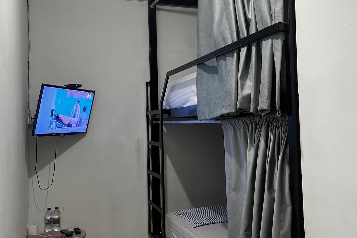 A bunk room with a television mounted on the wall, a small table with bottled water, and a ladder.