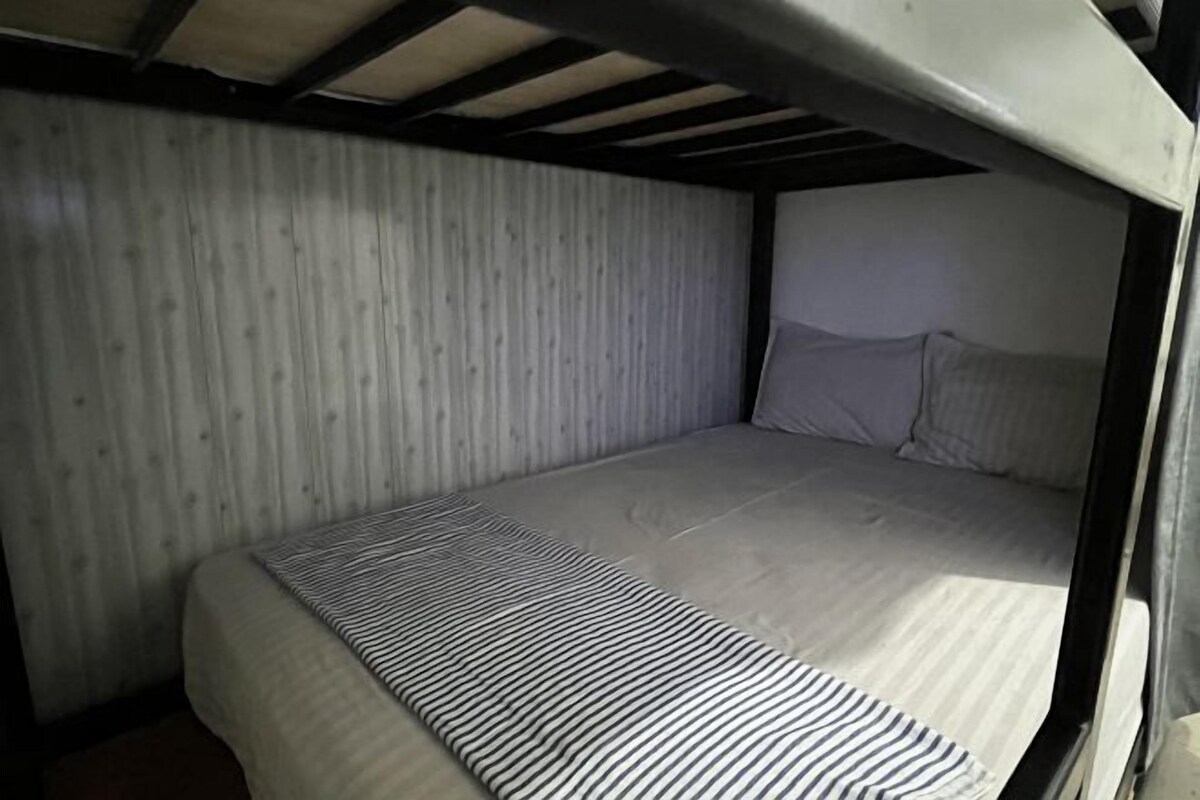 A bunk bed with a striped blanket and a wooden ceiling.