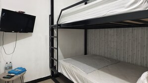 A bunk bed room with a TV mounted on the wall, a small table with a calculator and water bottles, and a tiled floor. - Ez Door (Yogyakarta)