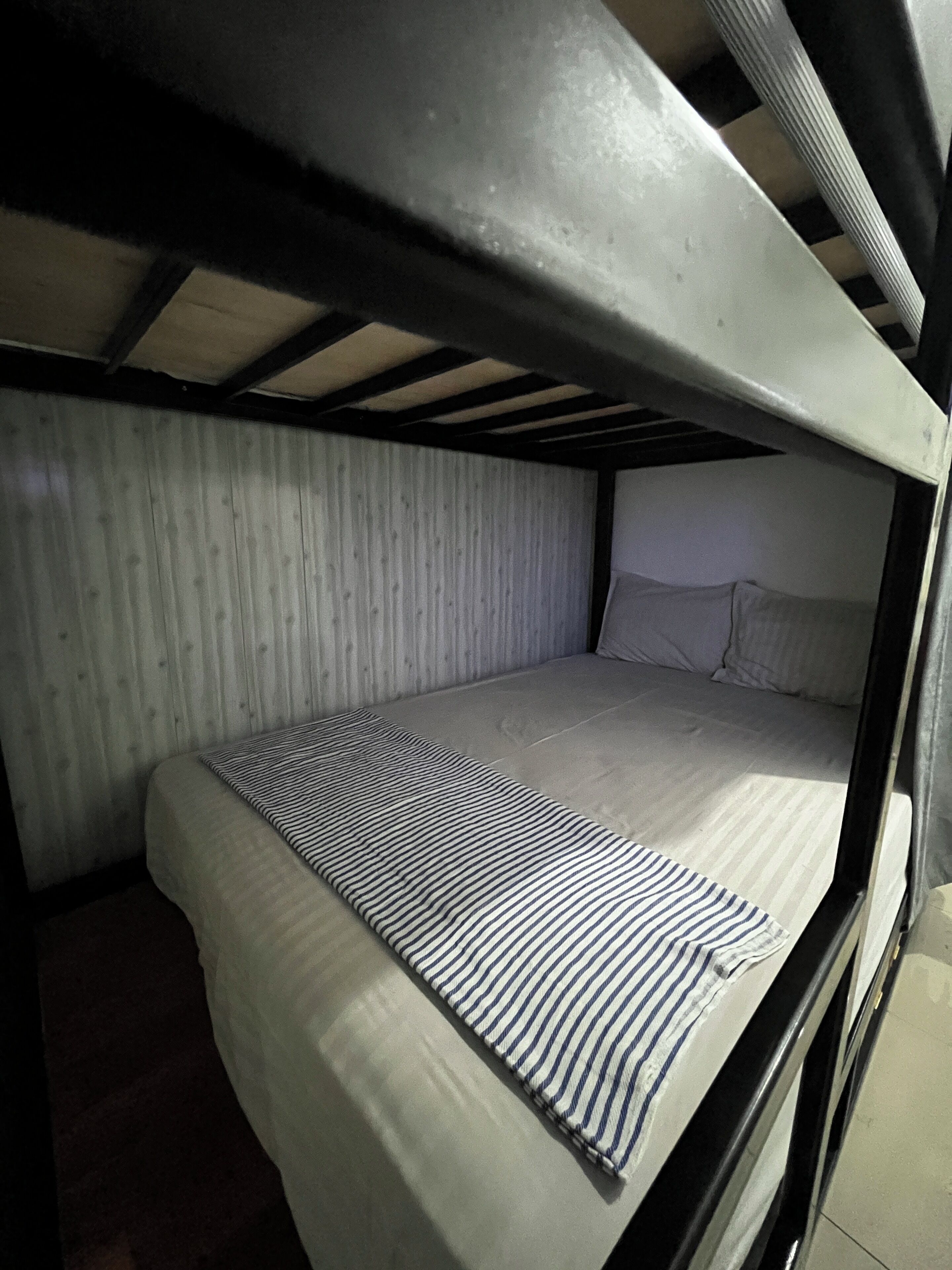 Una cama litera con una colcha a rayas y almohadas blancas en una habitación con paredes de madera y techo inclinado.