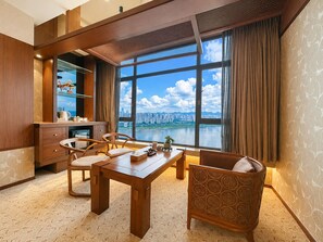 Habitación de hotel con un ventanal grande que ofrece vistas a la ciudad, un escritorio de madera, sillas y una cama.