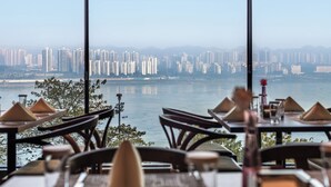 A restaurant with tables set for dining, overlooking a cityscape and a body of water. - Chongqing jiayu emperor hotel  (Chongqing)