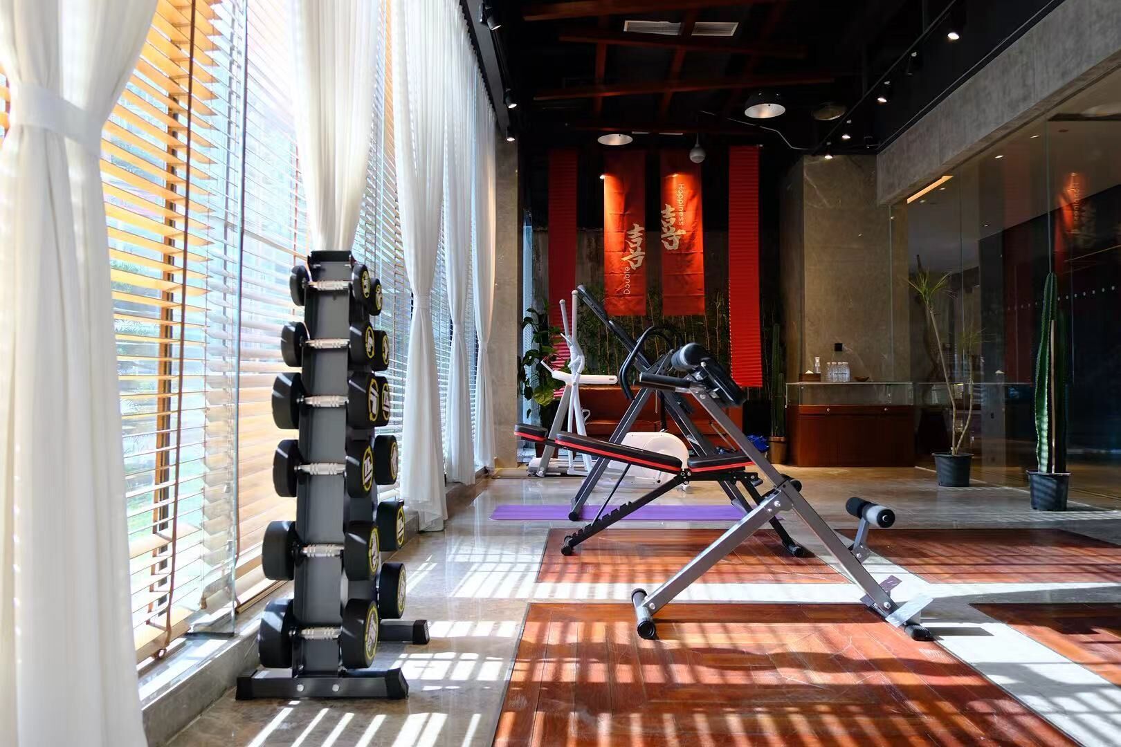 A gym with exercise equipment, large windows with blinds, and a reception area.