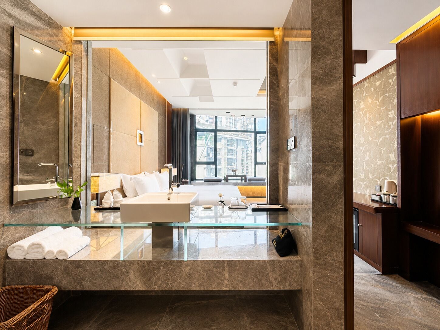 Un baño moderno con lavamanos de vidrio, un espejo grande y vistas de la ciudad a través de una ventana.