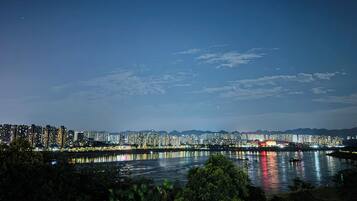A nighttime cityscape with a river reflecting lights, high-rise buildings, and mountains in the background.