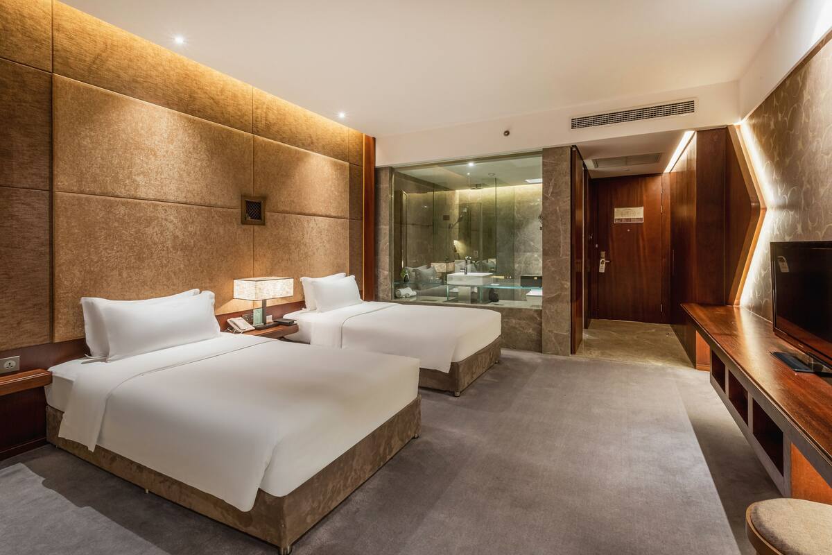 A hotel room with two beds, a TV, and a glass-enclosed shower area.