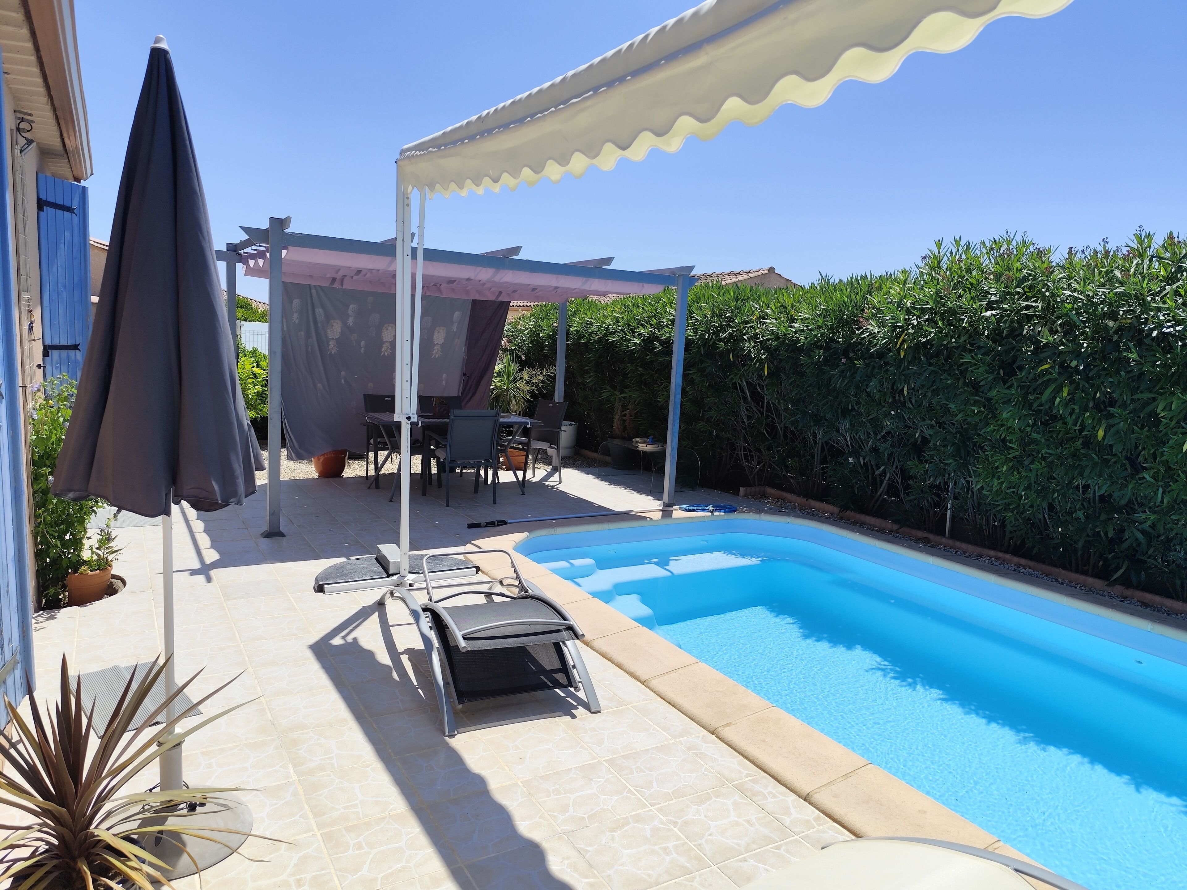 A swimming pool with a covered patio area, a table with chairs, and a potted plant.