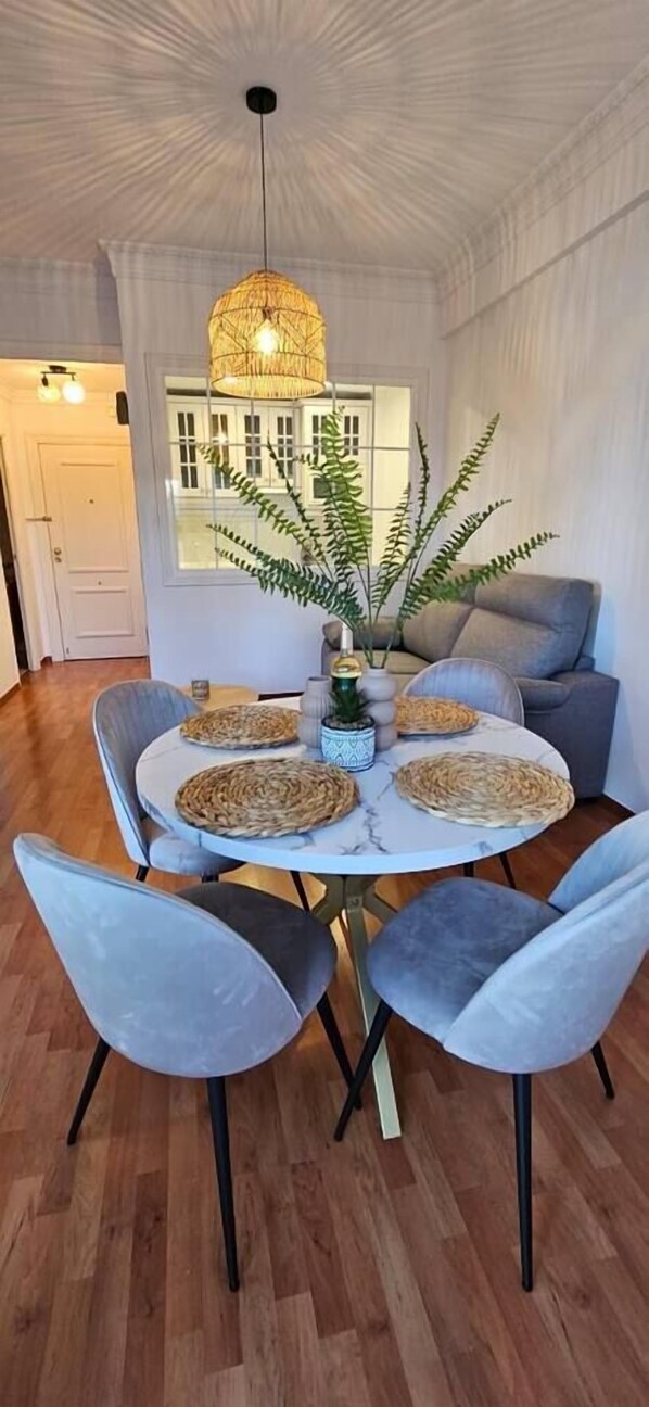 A dining area with a round table, grey upholstered chairs, a woven placemat, and a hanging light fixture.