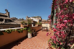 Une cour avec un sol recouvert de carreaux de terre cuite, des plantes en pot, une table et des chaises.
