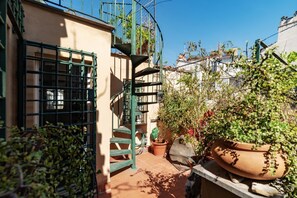A courtyard with a spiral staircase, potted plants, and a metal gate.