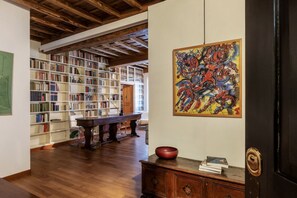 A room with a wooden floor, a bookshelf, a table, and a painting. - A Unique Penthouse with Spectacular Terraces in the Beating Heart of Rome (Roma)