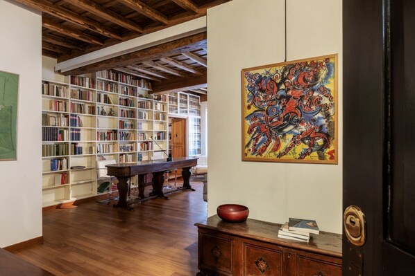 A room with a wooden floor, a bookshelf, a table, and a painting.