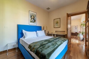 A bedroom with a blue headboard, a bed with white linens, a green throw blanket, and a framed picture on the wall.