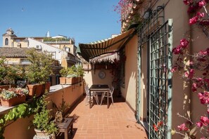 A narrow courtyard with a tiled floor, a table and chairs, potted plants, and a metal gate. - A Unique Penthouse with Spectacular Terraces in the Beating Heart of Rome (Roma)
