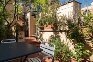 An outdoor patio with a table and chairs, surrounded by potted plants and a staircase. - A Unique Penthouse with Spectacular Terraces in the Beating Heart of Rome (Roma)
