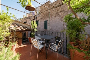 A patio with a table and chairs, surrounded by potted plants and a brick wall.
