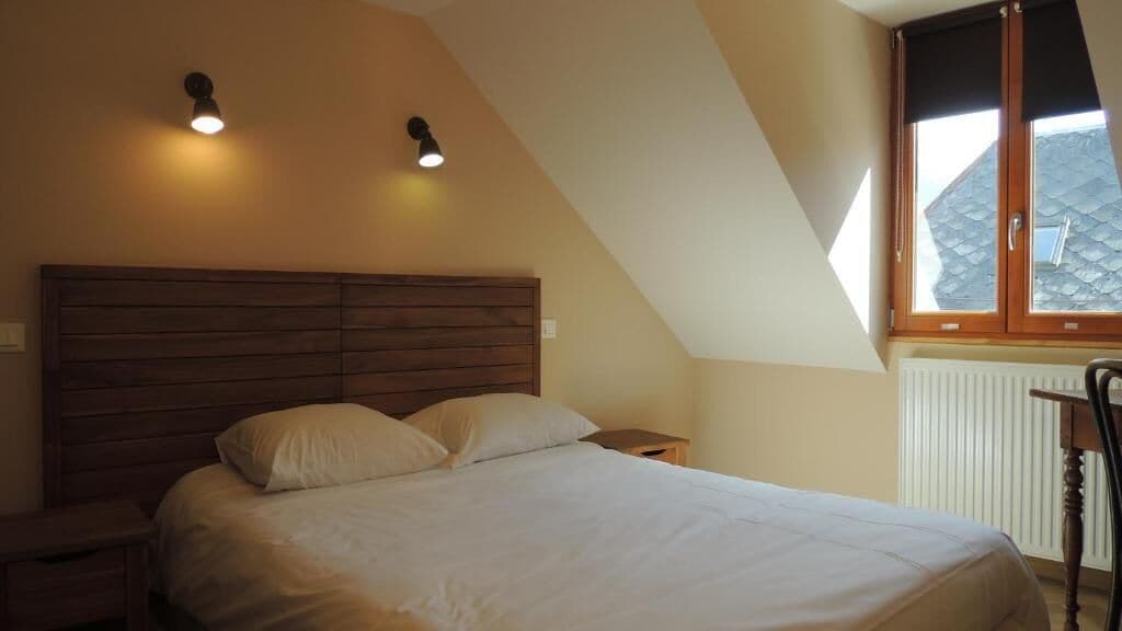 A bedroom with a wooden headboard, two bedside lamps, a window with a view of a roof, and a radiator.