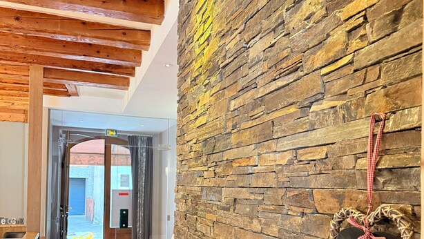 Un couloir avec un mur en pierre, des poutres en bois au plafond et une pancarte d’accueil en forme de cœur.