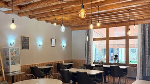 L’intérieur d’un restaurant avec des poutres en bois, des tables rondes et des chaises noires.