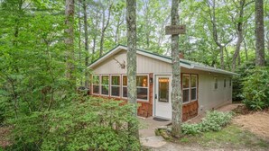 Une cabane dotée d’un grand porche à l’avant, entourée d’une forêt dense.