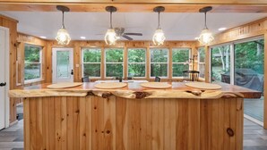 Un intérieur en bois avec un îlot central, de grandes fenêtres et des luminaires suspendus.