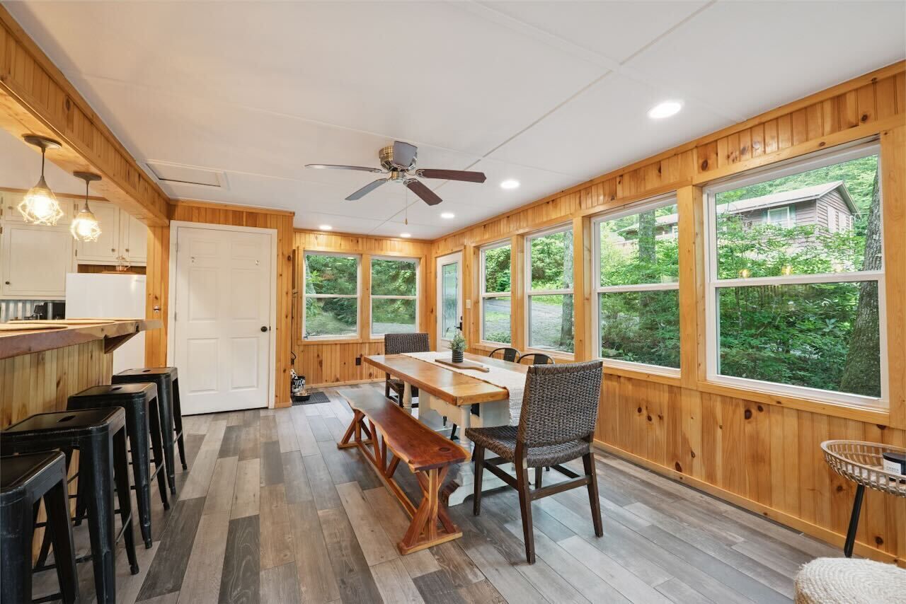 Une pièce spacieuse avec un plancher en bois, une table à manger avec des chaises, un banc et un ventilateur de plafond.