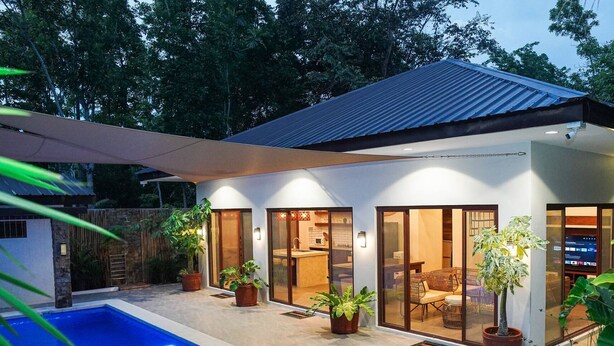 A modern house with a swimming pool, large glass doors, and potted plants.