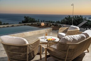 A patio with wicker chairs, a round table with a bottle and glasses, and a view of the ocean. - Villa Keras With Sea View (Viannos)