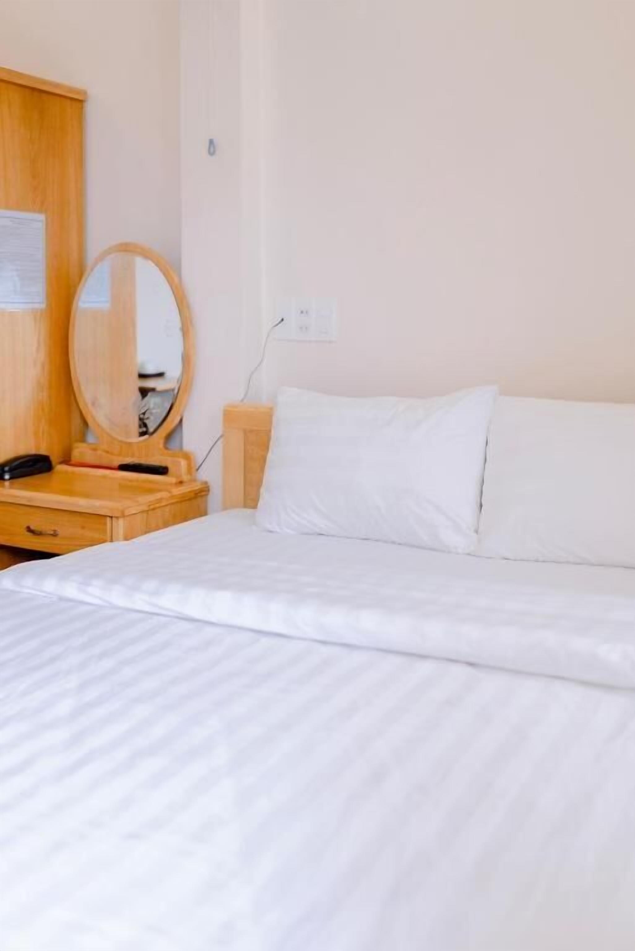 Une chambre d’hôtel avec un lit, une table de chevet en bois avec un téléphone, un miroir et une prise électrique au mur.