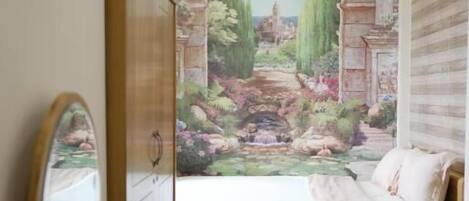 A bedroom with a mural of a garden scene, a wooden bed, a bedside table, and a mirror.
