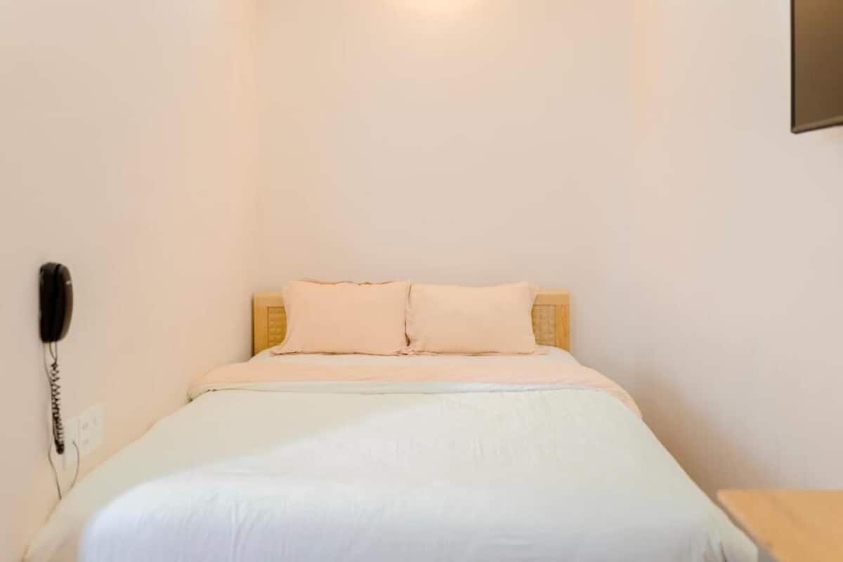 A single bed with a wooden headboard and two pillows, a bedside telephone, and a small wooden nightstand.