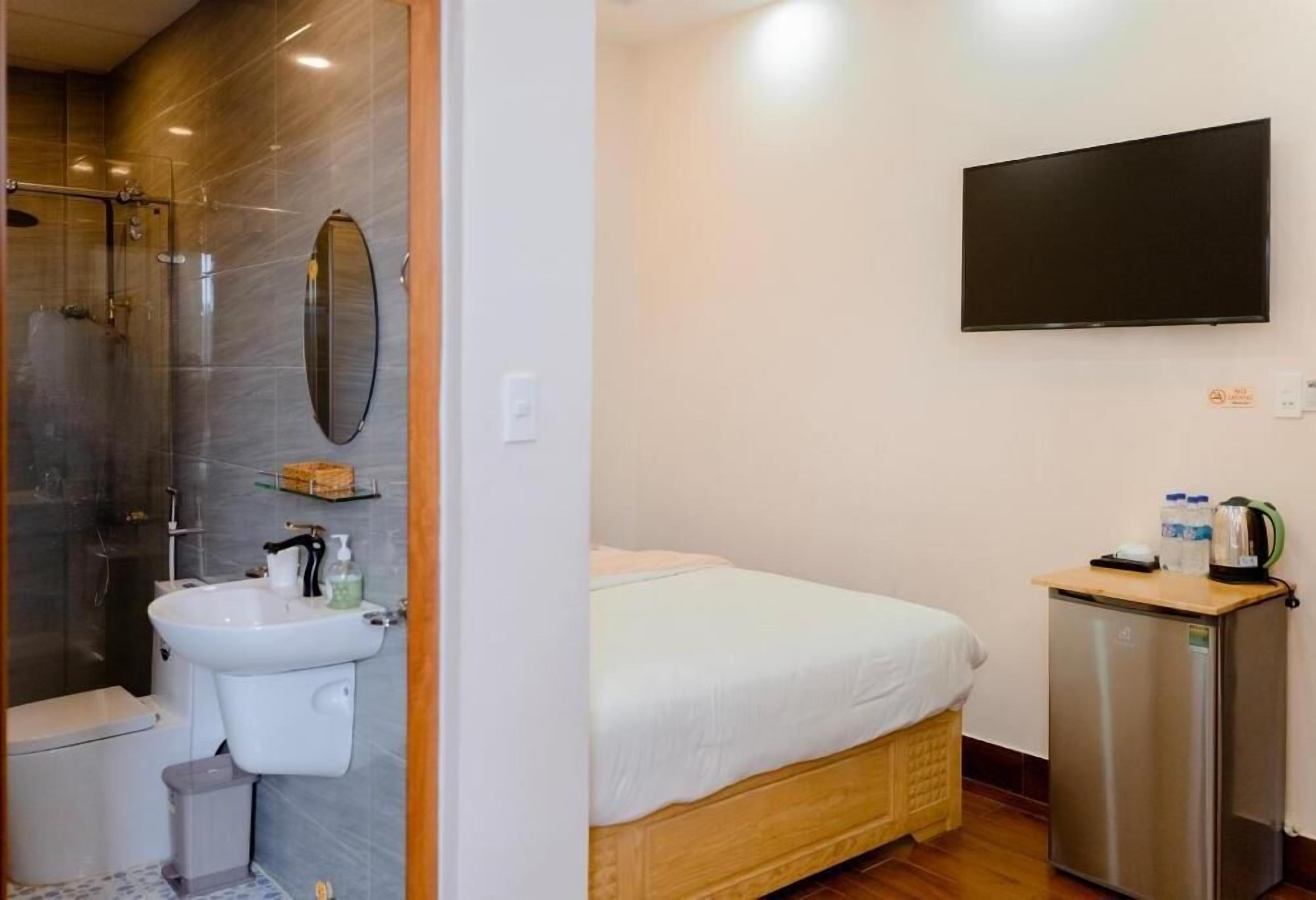 Et hotelværelse med bruser, håndvask, toilet, seng, fjernsyn og et lille køleskab.