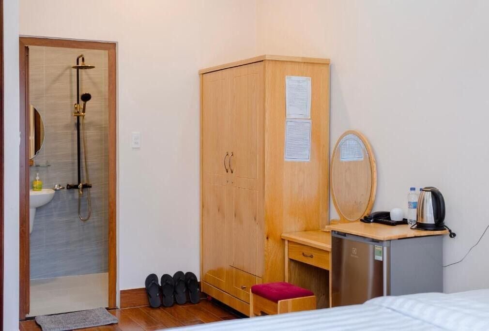 A compact room with a wooden wardrobe, a small desk with a mirror, a sink, and a shower.