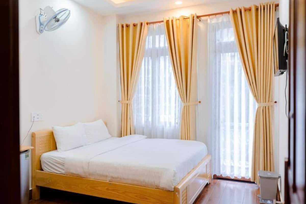 A bedroom with a wooden bed, white bedding, a wall-mounted fan, and curtains.