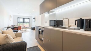 A modern kitchen with built-in appliances, a dining area with a table and chairs, and a sofa. - Spacious 1BR Apartment in Central Leeds (Leeds)