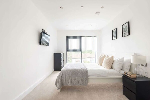 A bedroom with a bed, bedside table, lamp, and a window with blinds.