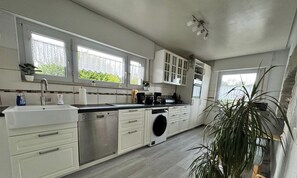 A modern kitchen with white cabinets, a dishwasher, a coffee maker, and a large window. - Holiday Home '2 Apartments in Refugium 2020' with Private Terrace, Private Garden and Wi-Fi (Marienheide)