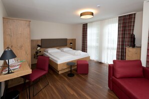 A hotel room with a wooden bed, a desk with a chair, a red sofa, and a TV on a wooden cabinet. - Landhotel Gasthof Krone (Kupferzell)