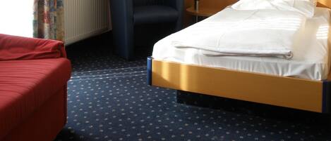 Ein Hotelzimmer mit einem Bett, einem roten Sofa, einem blauen Sessel, einem Gemälde an der Wand und einem Fenster mit Vorhängen.