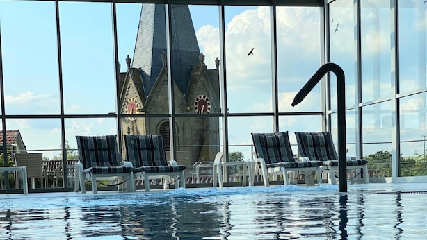 Una piscina interior con sillones de descanso y vista a una iglesia con reloj.