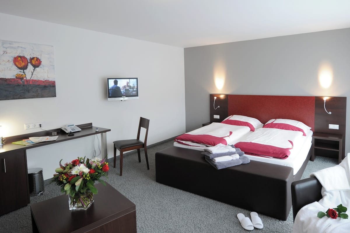 Habitació d'hotel amb llit, taules de nit, escriptori, cadira, televisió i un quadre penjat a la paret.