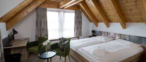 A room with a sloped ceiling, wooden beams, a bed, a desk, a chair, and a window with curtains.