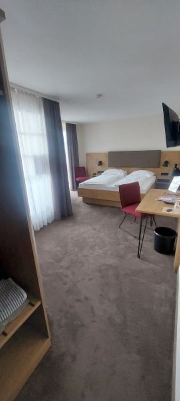 A hotel room with a bed, a desk, a chair, a TV, and a window with curtains. - Landhotel Gasthof Krone (Kupferzell)