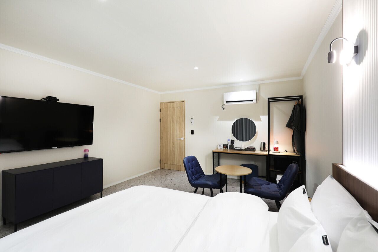 Habitación de hotel con cama, televisión, escritorio con silla, mesita pequeña y espejo.
