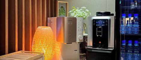 A modern kitchen with a coffee machine, a water dispenser, and a wooden side table with a lamp.