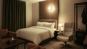 A hotel room with a large bed, a sitting area with a sofa and armchair, a desk with a lamp, and a coat rack. - Casa Incanto Hotel in Gumi (Gumi)
