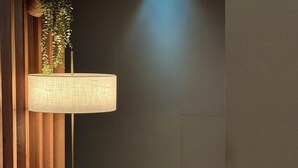 A modern bathroom with a wooden panel wall, a hanging plant, a round table with a lamp, and a towel rack. - Casa Incanto Hotel in Gumi (Gumi)