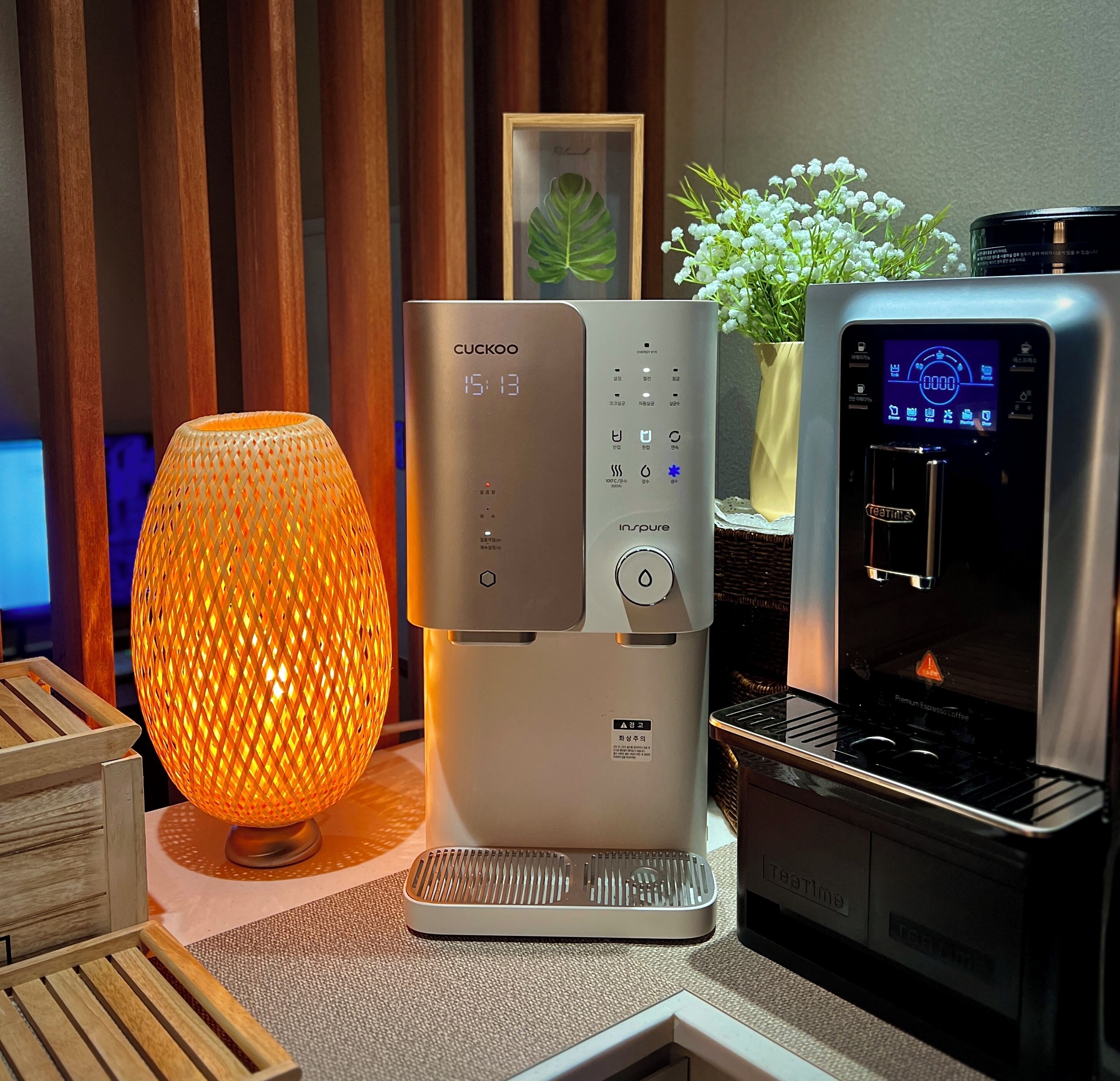 A modern kitchen with a Cuckoo coffee maker, a Teatime espresso machine, and a decorative orange lamp.